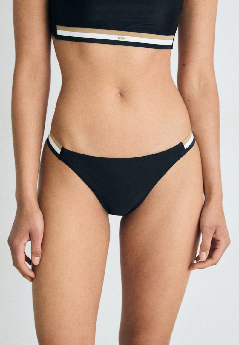 Μαύρο κάτω μέρος μπικίνι με χαμηλή μέση, διαθέτει λεπτές τιράντες με χρυσές, λευκές και μαύρες λεπτομέρειες στη ζώνη. Μαλακό, ελαστικό υλικό.