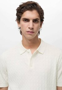 White polo shirt made of textured fabric with subtle cable-knit pattern. Features a classic collar and two buttons at the neck.