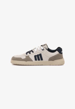 Low-top sneaker met beige en witte panelen, zwart "m" logo aan de zijkant, zwart-witte veters en beige rubberen zool.