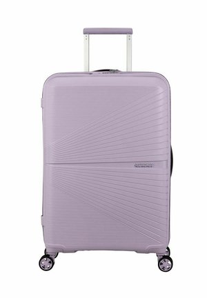 Valigia rigida di un leggero colore lavanda con scanalature diagonali, manico estensibile e quattro ruote nere per la mobilità. Logo del marchio visibile.