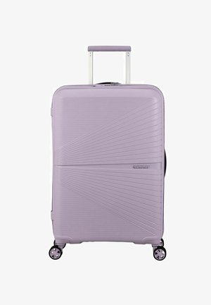 Valigia rigida di un leggero colore lavanda con scanalature diagonali, manico estensibile e quattro ruote nere per la mobilità. Logo del marchio visibile.