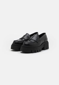 Mocassini in pelle nera con suola platform chunky e dettagli testurizzati. Finitura liscia, design slip-on e accenti di cucitura pronunciati.