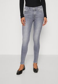 Vaqueros skinny grises de mezclilla, con una cintura de altura media, cinco bolsillos y una silueta ajustada. Llevados con flats negros de punta cuadrada.
