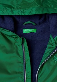 Chaqueta verde con cremallera y forro de polar azul marino. Presenta una cremallera plateada y un acento de logo. El tejido interior es suave, proporcionando calidez y comodidad.