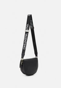 Borsa a tracolla in pelle nera con forma curva, dotata di una tracolla nera con il testo bianco "Valentino" e dettagli dorati sull'hardware.
