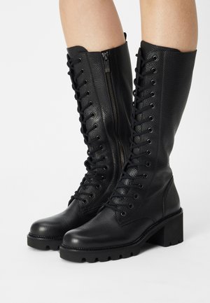 Zwarte leren kniehoge laarzen met veters aan de voorkant en een ritssluiting aan de zijkant, een gestructureerde afwerking, een blokhak en een profielen zool voor grip.