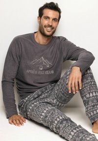 Szary longsleeve z grafiką "Après Ski Club", w parze z wzorzystymi szarymi spodniami piżamowymi z trójkątami i drzewami.