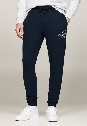 Pantalones de chándal azul marino con cintura elástica y cordón, que cuentan con un logo blanco en el muslo izquierdo y perneras ajustadas con puños acanalados.
