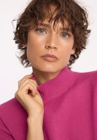 Fuksjowy sweter robiony na drutach z wysokim żebrowanym kołnierzem. Gładka tekstura, dopasowany krój, podkreślający luźny fason ramion.