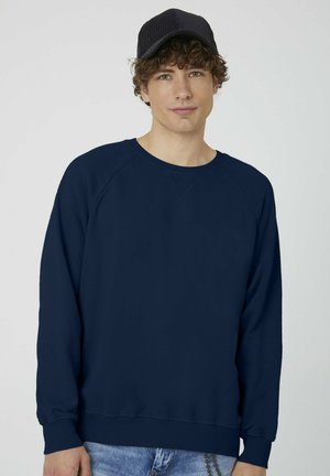 Dunkelblauer Sweatshirt mit Raglanärmeln, Rundhalsausschnitt und gerippten Bündchen. Aus weichem Stoff gefertigt, hat eine glatte Textur. Wird mit hellen Jeans getragen.