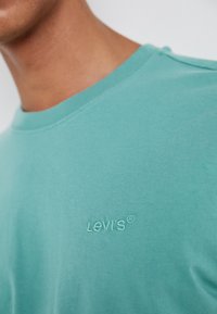 Turkis bomulls T-skjorte med rund hals og brodert "Levi's"-logo i matchende farge, som viser glatt tekstur og enkelt design.