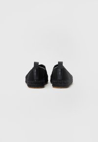 Espadrilles negras con suela de yute trenzado, que presentan un upper de cuero suave, dos tiradores y un acabado texturizado en los laterales.