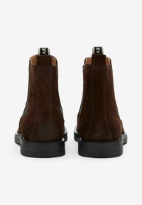 Bruine suède enkelboots met zwarte elastische zijkanten en stevige rubberen zolen. Opvallende tab aan de achterkant met branding.