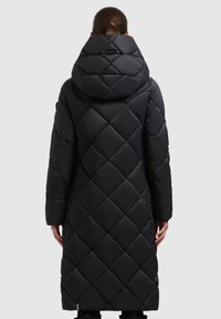 Palton lung negru, matlasat, cu glugă mare. Prezintă un model cu diamante, textură netedă și mâneci ajustate. Detalii de design minimalist.