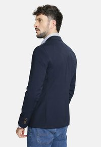 Blazer ajustado azul marino con hombros estructurados y puños abotonados, acompañado de una camisa de cuadro azul claro debajo.