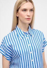 Camicia a maniche corte a righe blu e bianche con colletto e chiusura a bottoni, realizzata in tessuto leggero, caratterizzata da righe verticali uniforme.