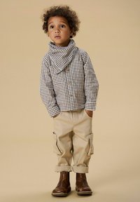Brown and white checkered shirt with button closure, beige cargo pants with cuffs, and brown leather boots. Light background.