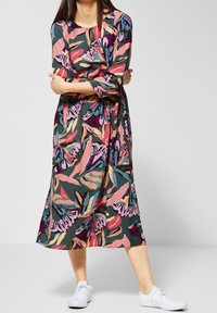 Midi šaty s květinovým vzorem a tříčtvrtečními rukávy; obsahují zelenou, růžovou, fialovou a žlutou barvu. Nosené s bílými teniskami.