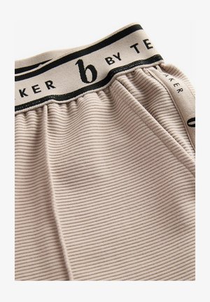 Tecido ribbed bej cu o textură moale, având o talie neagră cu branding "b by TE". Designul este strâns pentru o potrivire confortabilă.