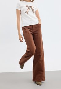 Vit t-shirt med en leopardmönstrad rosett, matchad med bruna bredbenta byxor i kordflod och olivgröna spetsiga klackar.