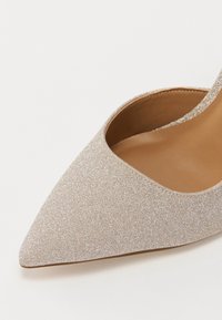 Chaussure à talons aiguilles beige pailletée avec un design à bout pointu et ouvert à l'arrière. Doublure intérieure lisse, texture subtile et silhouette épurée.