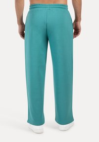 Turkusowe spodnie dresowe o luźnym kroju, z elastycznym pasem i gładką teksturą. Posiadają proste nogawki i prosty design.