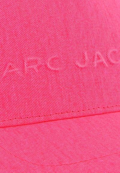 Roze stoffen pet met een zachte textuur, voorzien van een reliëf logo "MARC JACOBS" en een gestructureerde rand. Stiksels zichtbaar langs de randen.