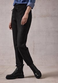 Sorte suede joggerbukser med elastisk talje, sidelommer og tapered ben, parret med sorte ankelstøvler med teksturerede såler.