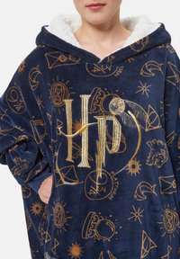 Felpa oversized con cappuccio di colore blu navy, con un morbido rivestimento interno bianco. Presenta il logo dorato "HP" e vari simboli magici in un motivo ripetuto.
