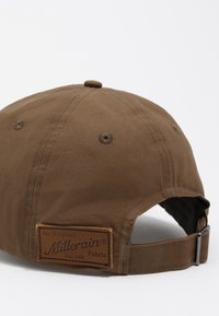 Gorra marrón hecha de tela Millerain, con una etiqueta de parche de cuero, correa ajustable y orificios de ventilación cerca de la parte superior.