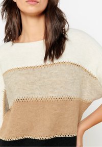 Sweter dziany w kremowe, beżowe i czarne paski. Zdobiony dekoracyjną złotą koronką na krawędziach; luźny, swobodny krój.