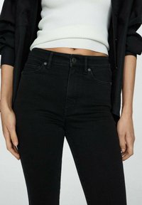 Mustat farkut, joissa on istuva muotoilu, vetoketjukiinnitys, etutaskut ja huomaamaton ompelu. Sileä rakenne.