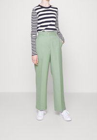 Pantaloni larghi verde realizzati in tessuto morbido, con vita alta e dettagli di pieghe. Abbinati a una maglietta a maniche lunghe a righe blu navy e bianche.