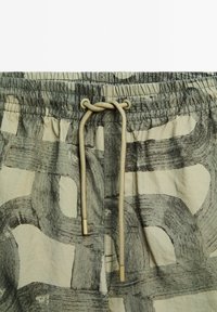 Leichte Shorts in Beige mit abstrakten dunkelgrauen Mustern, versehen mit einem hellbraunen Kordelzug mit Metallenden.