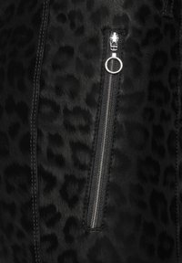 Tissu en fausse fourrure noire avec un motif léopard discret, comportant une fermeture éclair argentée et un détail de tirette de fermeture éclair circulaire.