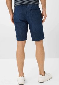 Shorts in denim blu scuro con vita elasticizzata, tasca posteriore e orli risvoltati, abbinati a sneaker bianche.