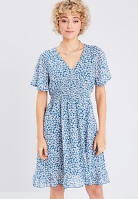 Robe florale bleue avec un décolleté en V, de courtes manches flottantes, une taille smockée et un ourlet froncé, décorée de petits motifs floraux blancs.