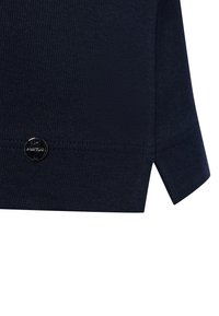 Marineblaue Rippstruktur mit seitlichen Schlitzen am Saum. Kleines metallisches Logodetail in der Nähe der Naht in der unteren linken Ecke.