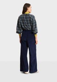 Camicia a quadri, oversize, con maniche a sbuffo, pantaloni a gamba larga in corduroy blu scuro e colletto giallo a contrasto.