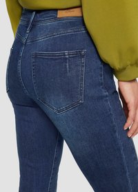 Dunkelblaue Jeans im Slim Fit, mit hoher Taille, Gesäßtaschen und einem lederartigen Markenpatch auf der Rückseite. Weiche Denim-Textur.
