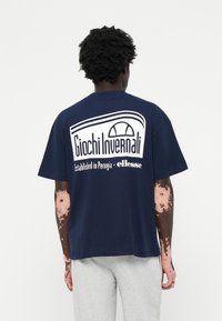 Mørkeblå bomulds t-shirt med et hvidt grafisk print på ryggen, der står "Giochi Invernali" og "Established in Perugia · ellesse."