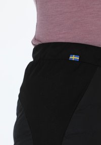 Zwarte broek met een gestructureerd oppervlak en een getailleerd ontwerp, voorzien van een klein Zweeds vlaggenlabel nabij de taille.