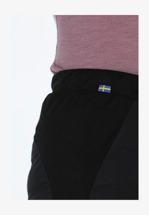 Czarne spodnie z teksturowaną powierzchnią i dopasowanym krojem, ozdobione małą naszywką z flagą szwedzką blisko talii.