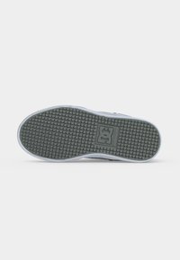 Semelle d'une basket avec un motif en grille et un logo rectangulaire central sur un fond gris clair.