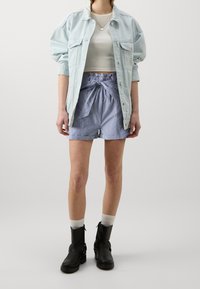 Světle modrá denimová oversized bunda, padnoucí bílý cropped top, pruhované kraťasy s vysokým pasem a zavazováním, černé kotníkové boty a bílé ponožky.
