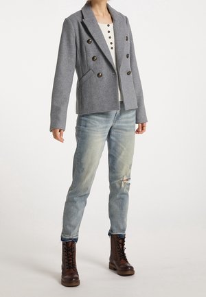 Person wearing a grey double-breasted blazer, white shirt with buttons, light ripped jeans, and brown lace-up boots on a white background.