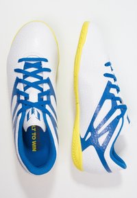 Vita atletiska skor med blå accenter, texturerad ovandel, gul sula och blå snören. Lättviktssdesign med distinkta mönster och stödjande struktur.