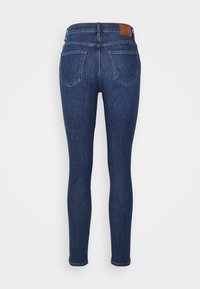 Jeans ajustados en denim azul oscuro, con una textura suave, diseño de cinco bolsillos y un detalle de cinturón de cuero marrón.