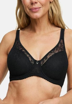 Vrouw draagt een zwarte kanten beha met brede bandjes en een klein zilverkleurig hangertje in het midden aan de voorkant.