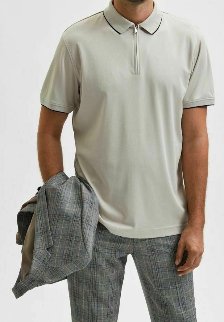 Polo gris clair avec col zippé, manches courtes et bord noir contrastant, assorti avec un pantalon à carreaux gris et un blazer coordonné.